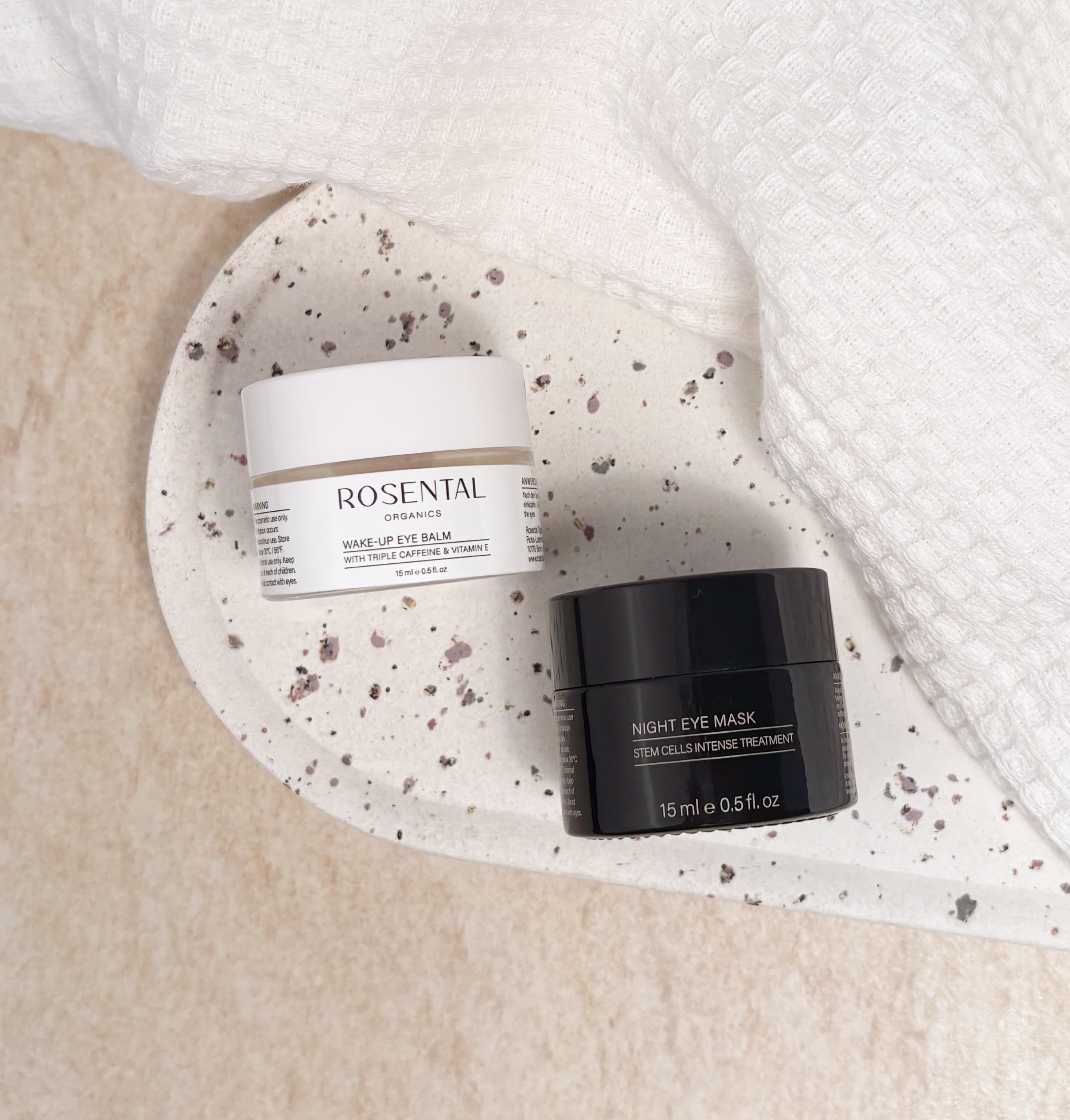 Die Wake Up Eye Balm Produkte von Rosental Organics für eine vitalisierende Augenpflege liegen mittig auf einem weißen Tablett. 