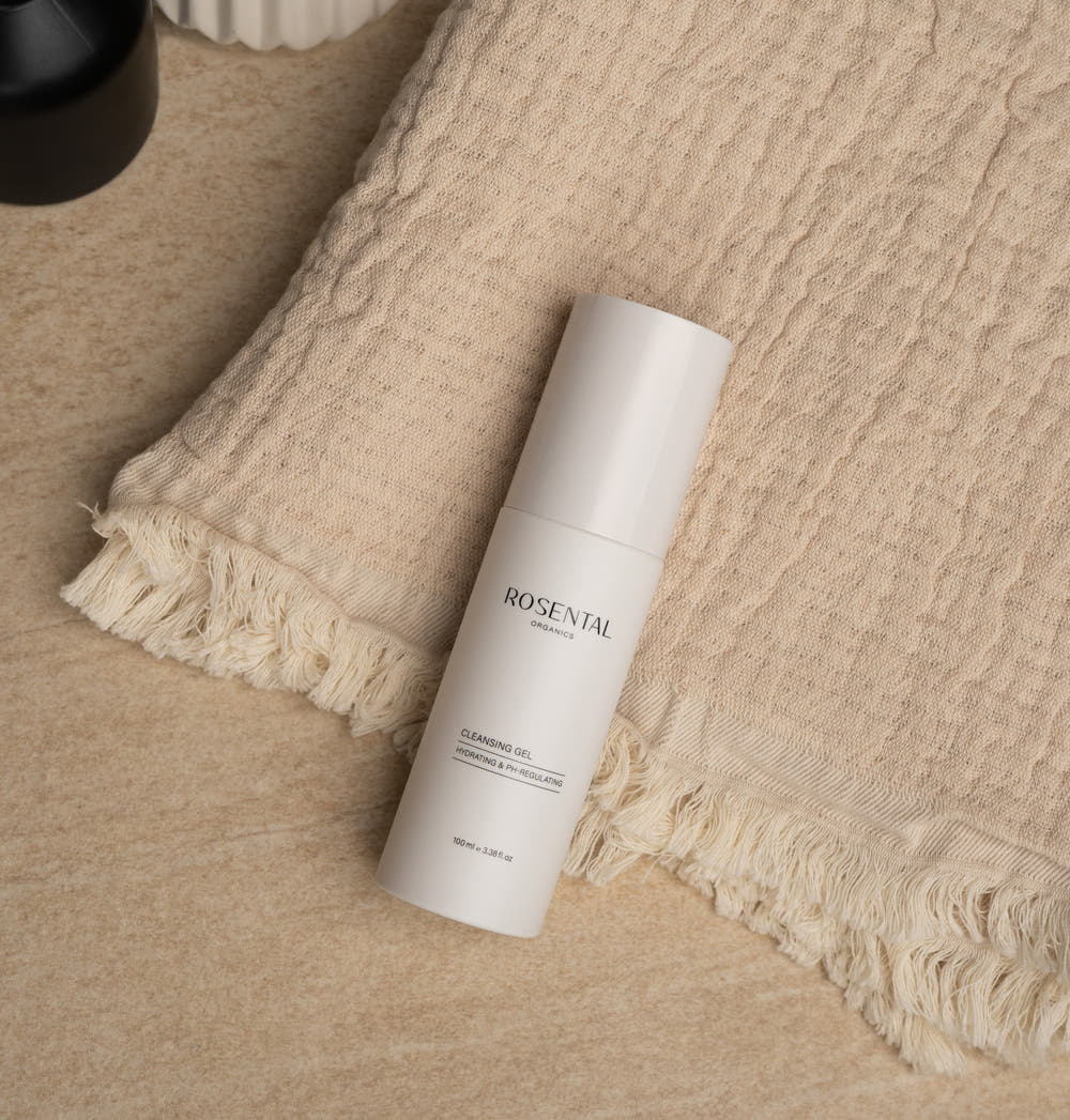Cleansing Gel in beigefarbener Verpackung, welches stilvoll platziert auf einem Handtuch liegt, das sich auf einer glatten Marmoroberfläche befindet.