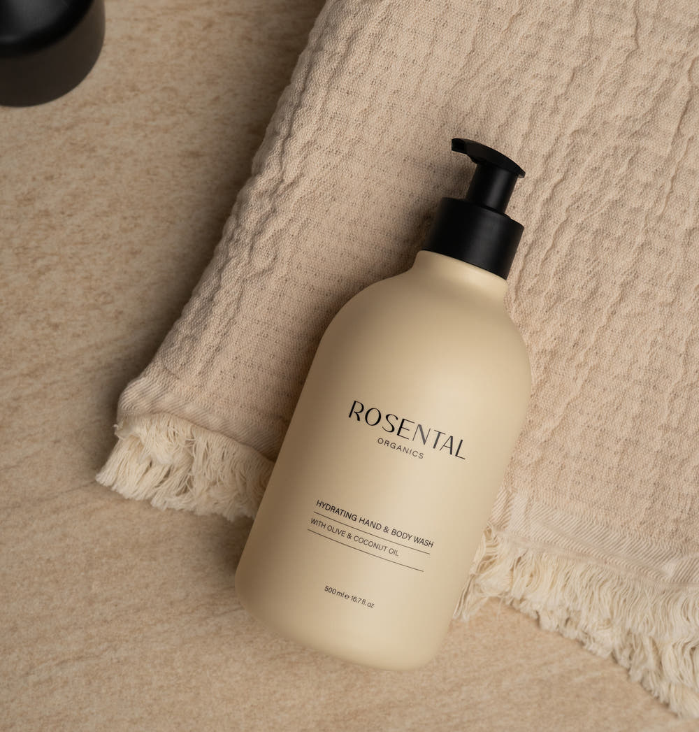 Hydrating Hand & Body Wash in beigefarbenem Pumpspender, liegend auf einem beigen Handtuch auf Marmoroberfläche.